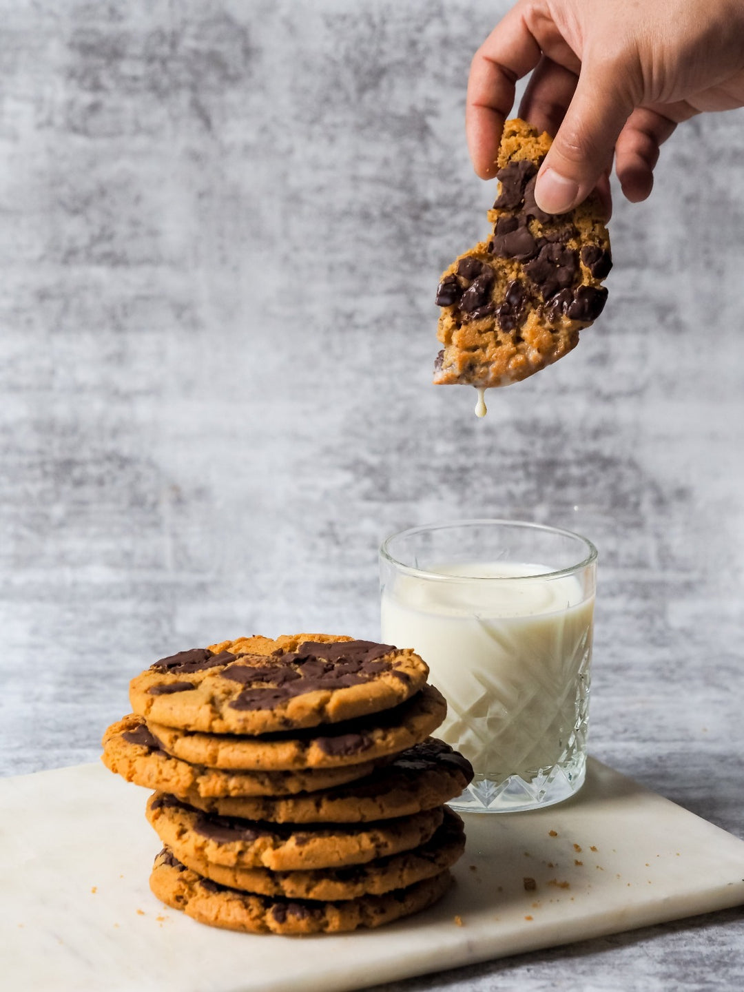 Photo of Gluten Free Cookies stacked on a board with half a cookie dipped into a glass of milk